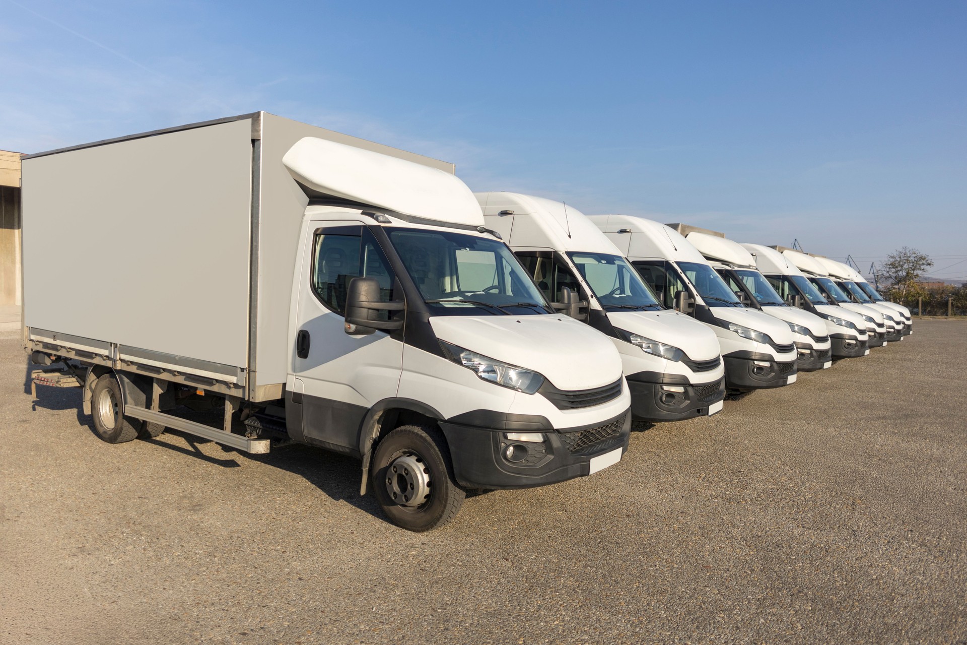 Fleet of white delivery trucks parked in a row at a logistics yard under clear blue sky